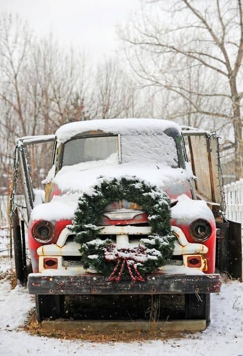 Caminhão Chevrolet antigo e abandonado, coberto de neve e com uma grande guirlanda de Natal enfeitando-o na dianteira 