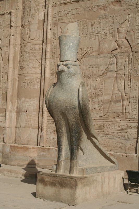 Estátua do deus egípcio Horus. Na parede, sua representação em forma humana