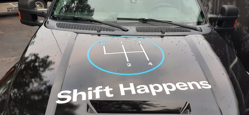 Caminhão de serviço da Hagerty com a decoração Shift Happens e esquema de marchas de câmbio manual. Bom humor com piada  "shit happens" e sempre apoiando a arte de trocar de marcha quando se quer
